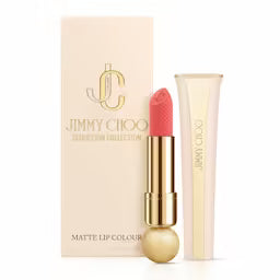 "Luxury Jimmy Choo Seduction Collection Lipstick in the shade Coral Sunset. The weighted gold-tone jewel case is open, showing a warm, sun-baked coral lipstick bullet with the signature python-skin embossed pattern.